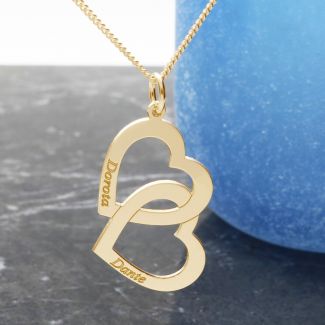Two gold interlinking hearts pendant hanging vertically and angled sideways. Engraved with one name on each heart on an optional gold curb chain